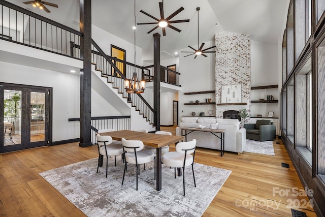 dining room featuring ceiling fan with notable chandelier, a fireplace, light hardwood / wood-style flooring, and high vaulted ceiling