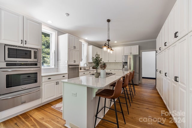 kitchen featuring appliances with stainless steel finishes, light hardwood / wood-style floors, white cabinets, a kitchen island, and pendant lighting