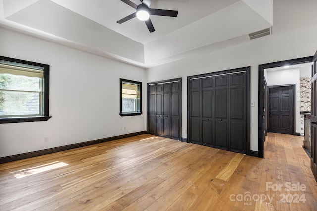 unfurnished bedroom featuring multiple closets, light hardwood / wood-style floors, a raised ceiling, and ceiling fan