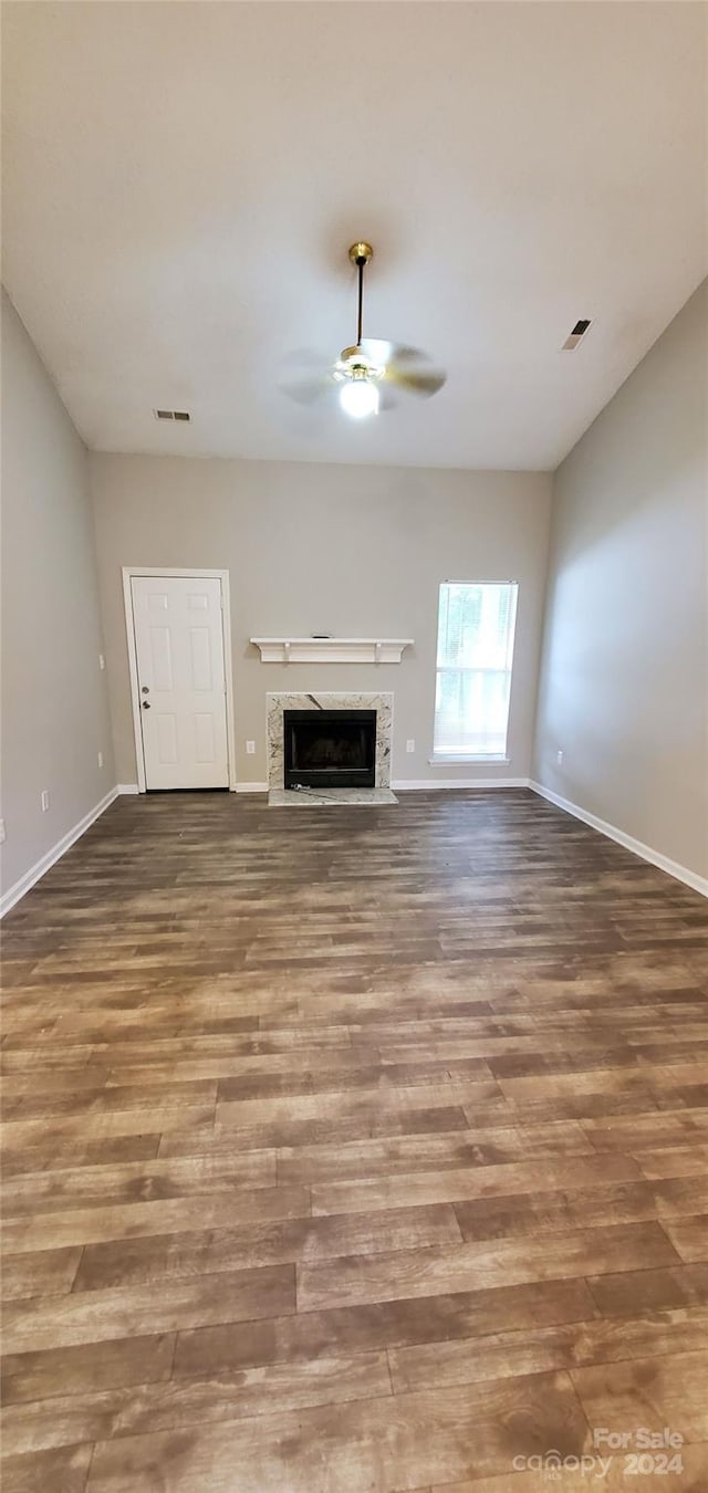 unfurnished living room with a high end fireplace, visible vents, baseboards, wood finished floors, and a ceiling fan