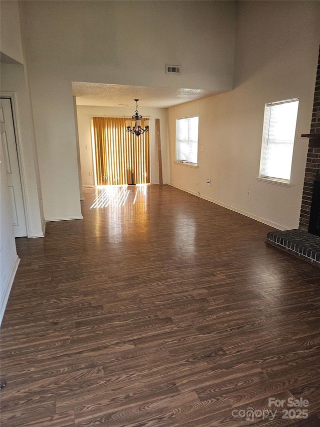 unfurnished living room featuring a notable chandelier, dark wood-type flooring, and a fireplace