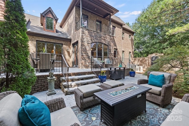 back of house with a patio, a balcony, and an outdoor living space with a fire pit