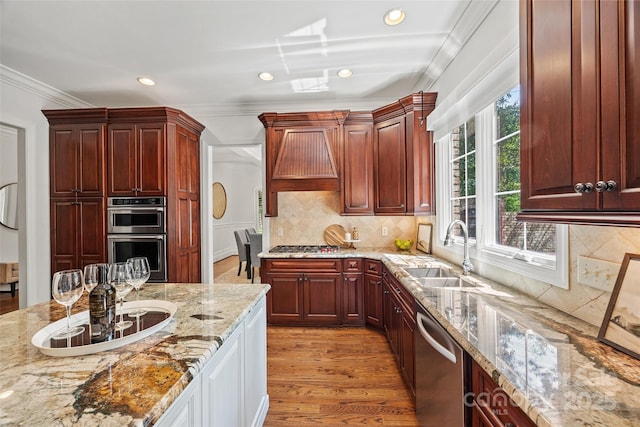 kitchen with appliances with stainless steel finishes, sink, light stone counters, crown molding, and light hardwood / wood-style flooring