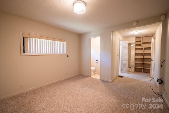 unfurnished bedroom with carpet flooring, a textured ceiling, a spacious closet, and ensuite bathroom