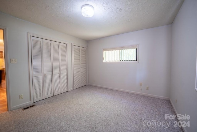 unfurnished bedroom featuring a textured ceiling, carpet flooring, and two closets