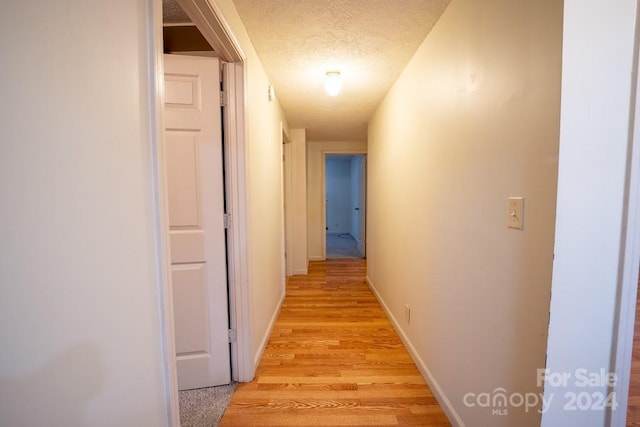 corridor with a textured ceiling and light wood-type flooring