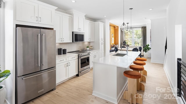 kitchen featuring a sink, premium appliances, white cabinets, and a kitchen island with sink