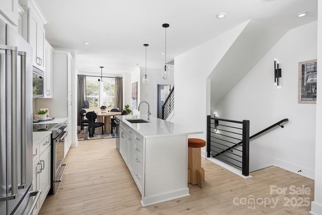 kitchen featuring a sink, hanging light fixtures, appliances with stainless steel finishes, white cabinets, and an island with sink