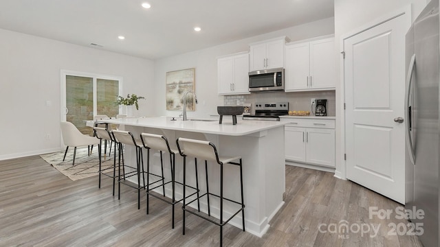 kitchen with decorative backsplash, appliances with stainless steel finishes, a kitchen breakfast bar, a kitchen island with sink, and a sink