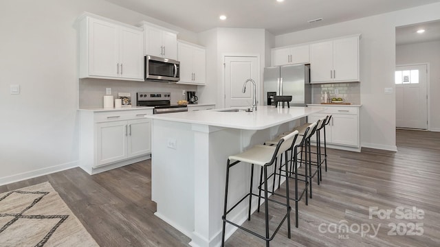 kitchen with stainless steel appliances, white cabinets, a sink, wood finished floors, and a kitchen breakfast bar