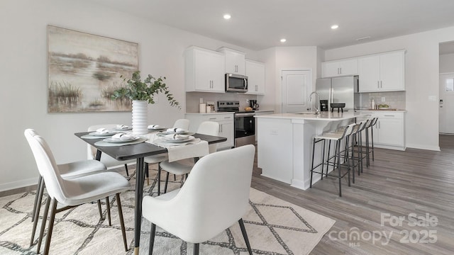 kitchen featuring a center island with sink, decorative backsplash, a breakfast bar, stainless steel appliances, and light countertops