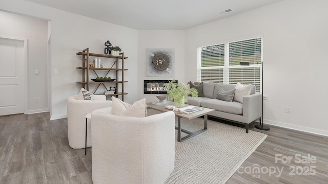 living area featuring baseboards, visible vents, wood finished floors, and a glass covered fireplace