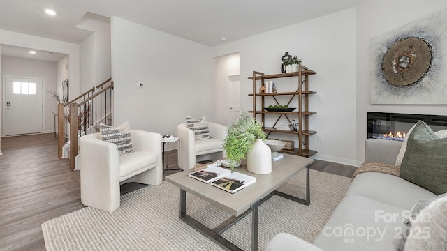 living area with baseboards, a glass covered fireplace, stairway, wood finished floors, and recessed lighting