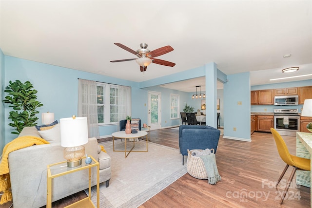 living room with light wood-type flooring and ceiling fan with notable chandelier