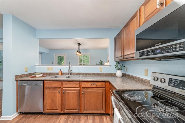 kitchen featuring decorative light fixtures, stainless steel appliances, sink, and light hardwood / wood-style flooring