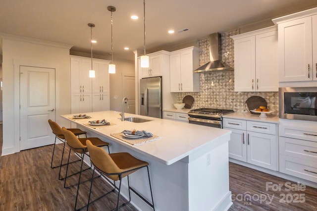 kitchen with white cabinetry, stainless steel appliances, wall chimney range hood, decorative backsplash, and a kitchen island with sink