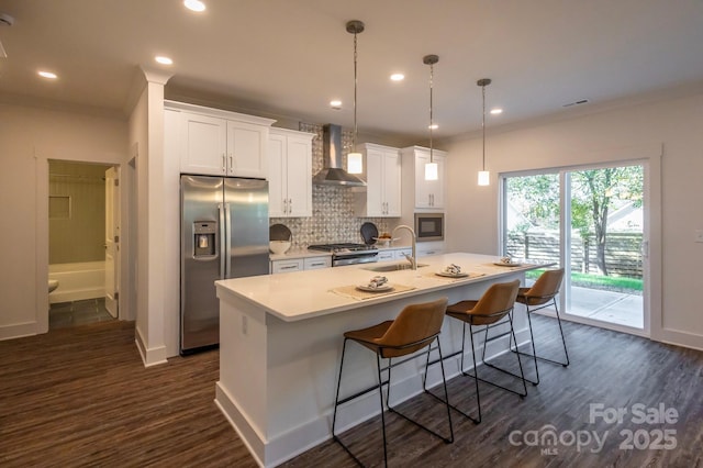 kitchen featuring wall chimney exhaust hood, sink, stainless steel appliances, and an island with sink