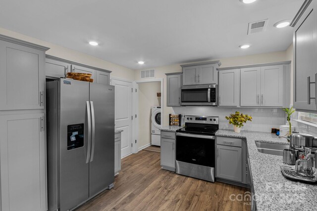 kitchen featuring light stone countertops, appliances with stainless steel finishes, tasteful backsplash, washer / dryer, and dark hardwood / wood-style floors