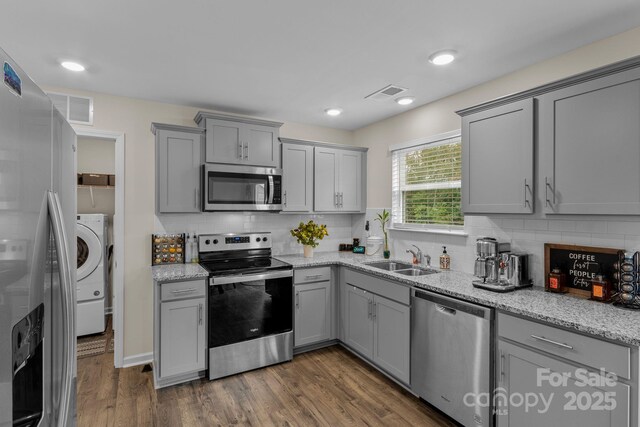 kitchen featuring sink, dark wood-type flooring, light stone counters, gray cabinets, and appliances with stainless steel finishes