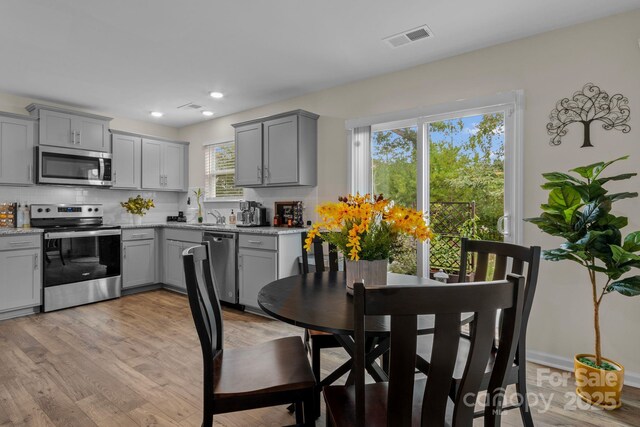 kitchen featuring gray cabinetry, light stone counters, backsplash, and appliances with stainless steel finishes