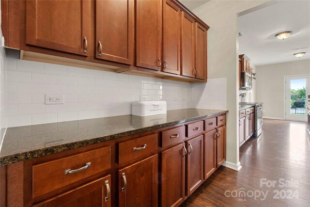 kitchen featuring appliances with stainless steel finishes, tasteful backsplash, dark hardwood / wood-style flooring, and dark stone counters