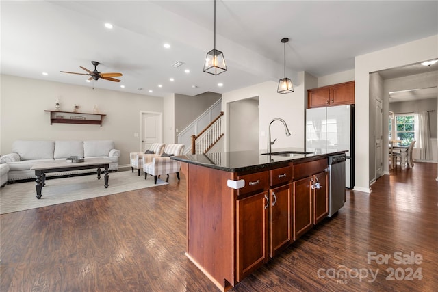 kitchen featuring dark stone counters, an island with sink, ceiling fan, sink, and dark hardwood / wood-style floors