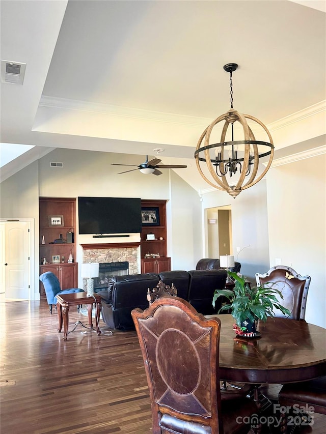 dining area with built in shelves, dark hardwood / wood-style flooring, a fireplace, ceiling fan with notable chandelier, and ornamental molding