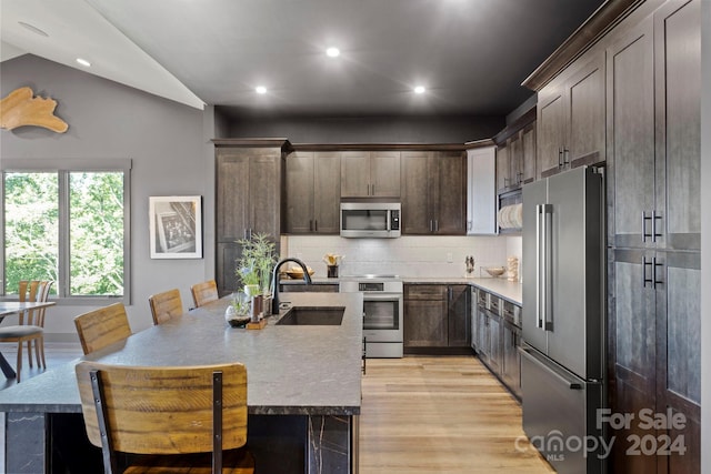 kitchen with vaulted ceiling, light hardwood / wood-style flooring, backsplash, stainless steel appliances, and sink