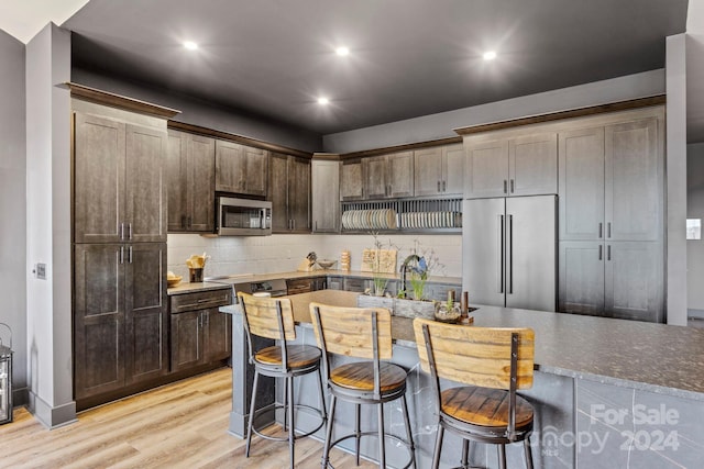 kitchen with light hardwood / wood-style flooring, appliances with stainless steel finishes, a kitchen bar, an island with sink, and decorative backsplash