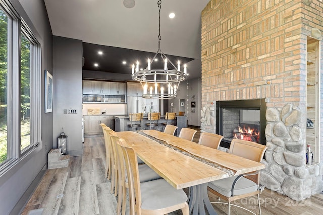 dining room featuring a healthy amount of sunlight, light hardwood / wood-style flooring, a notable chandelier, and a stone fireplace