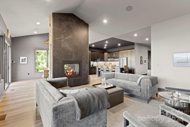 living room featuring vaulted ceiling, a tile fireplace, and light hardwood / wood-style floors