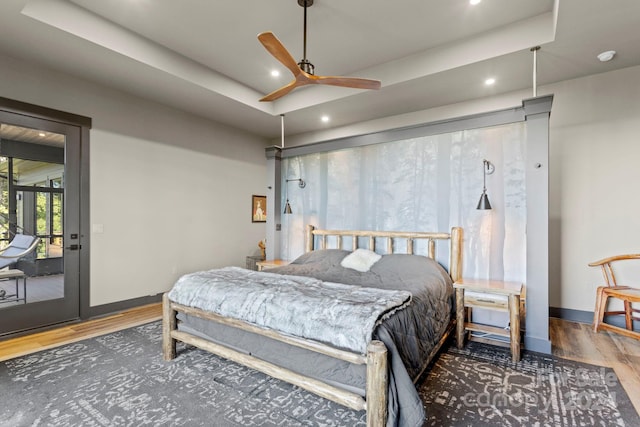 bedroom with access to exterior, ceiling fan, wood-type flooring, and a tray ceiling