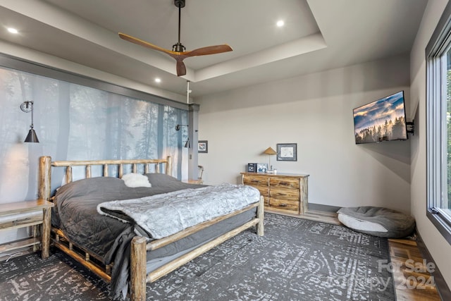 bedroom with ceiling fan, dark hardwood / wood-style floors, and a tray ceiling