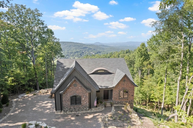 view of front of house featuring driveway, a forest view, a mountain view, roof with shingles, and brick siding