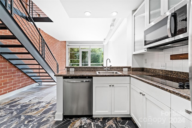 kitchen with white cabinets, stainless steel appliances, sink, brick wall, and dark stone counters