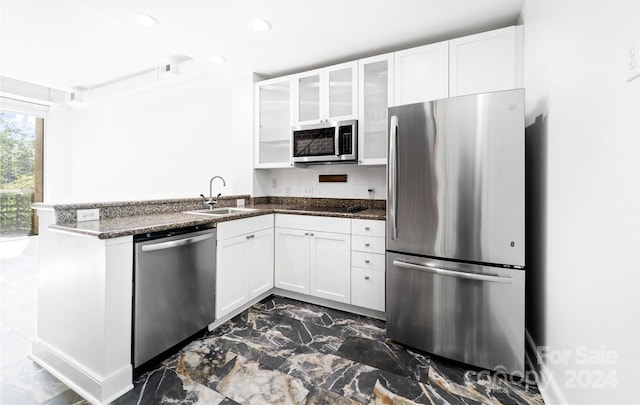 kitchen with appliances with stainless steel finishes, white cabinetry, kitchen peninsula, and sink