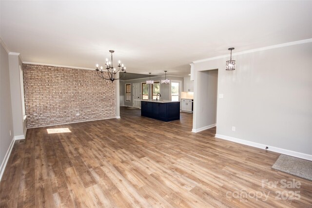 unfurnished living room featuring wood-type flooring, crown molding, sink, brick wall, and a chandelier