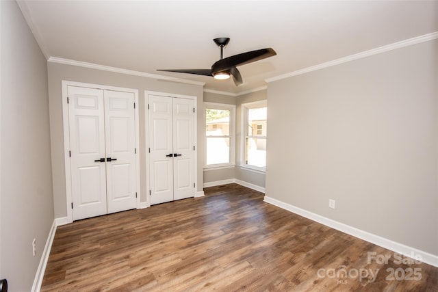 unfurnished bedroom featuring crown molding, dark hardwood / wood-style floors, two closets, and ceiling fan