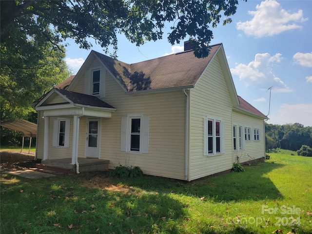 view of front of home with a front lawn, a porch, roof with shingles, a chimney, and a carport