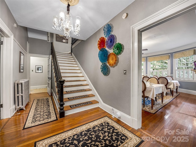 stairs with hardwood / wood-style floors, radiator heating unit, and a chandelier