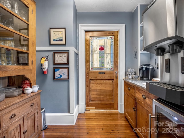 interior space featuring a textured ceiling, light hardwood / wood-style floors, wine cooler, and light stone countertops