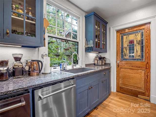 bar featuring dishwasher, light hardwood / wood-style floors, blue cabinets, dark stone countertops, and sink