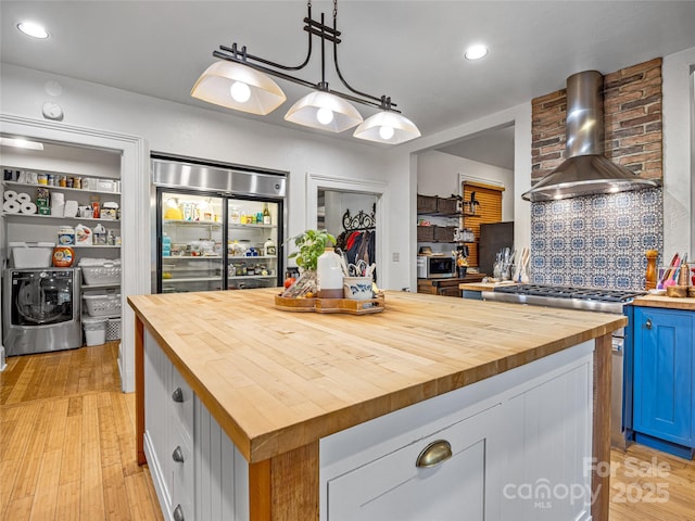 kitchen with a kitchen island, decorative light fixtures, wooden counters, and wall chimney exhaust hood