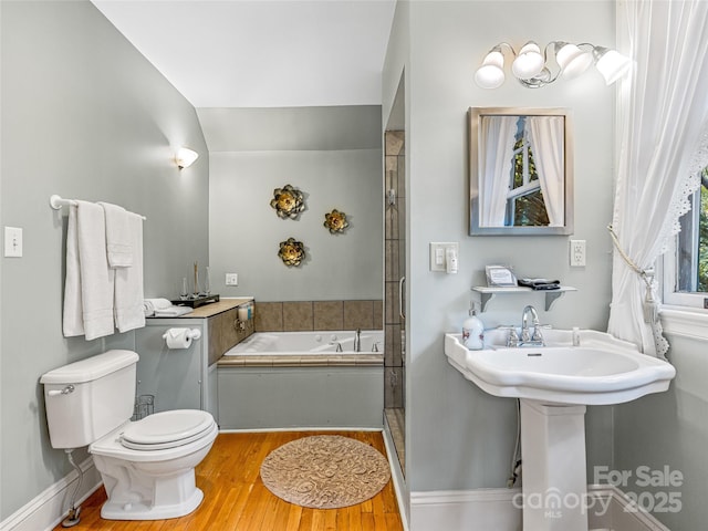 bathroom featuring lofted ceiling, hardwood / wood-style flooring, toilet, and a tub to relax in