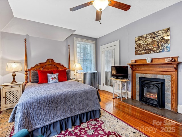 bedroom with radiator, a tile fireplace, ceiling fan, and hardwood / wood-style flooring