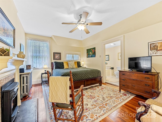 bedroom with hardwood / wood-style floors, connected bathroom, ceiling fan, and a wood stove