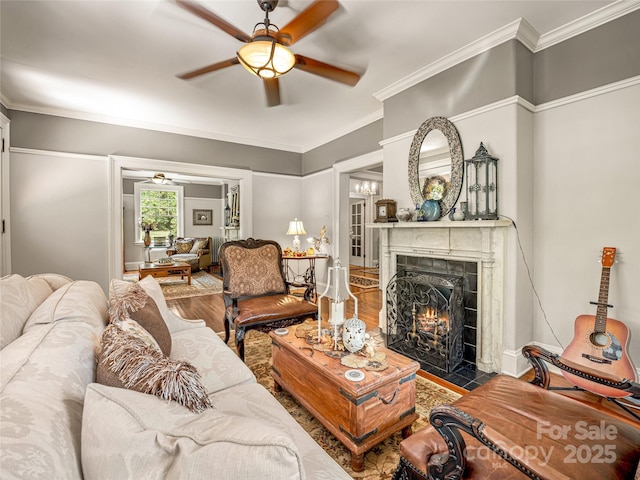 living room with a tiled fireplace, hardwood / wood-style floors, ornamental molding, and ceiling fan