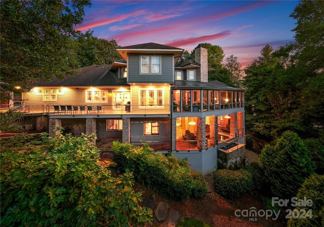 back house at dusk featuring a balcony and a sunroom