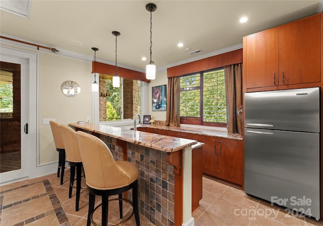 kitchen with stainless steel refrigerator, light stone countertops, light tile patterned floors, pendant lighting, and crown molding