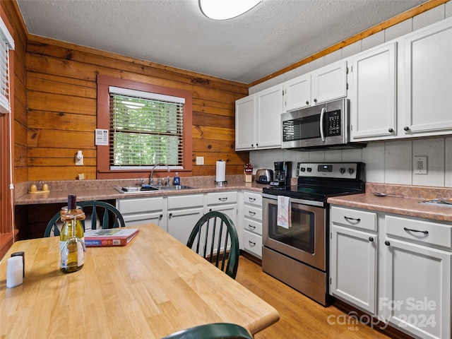 kitchen featuring appliances with stainless steel finishes, white cabinetry, sink, and wooden walls